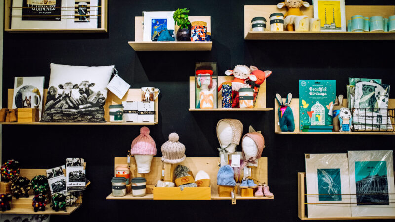 A black wall with wooden shelves. Shelves contain books, knitwear and candles. A variety of objects.