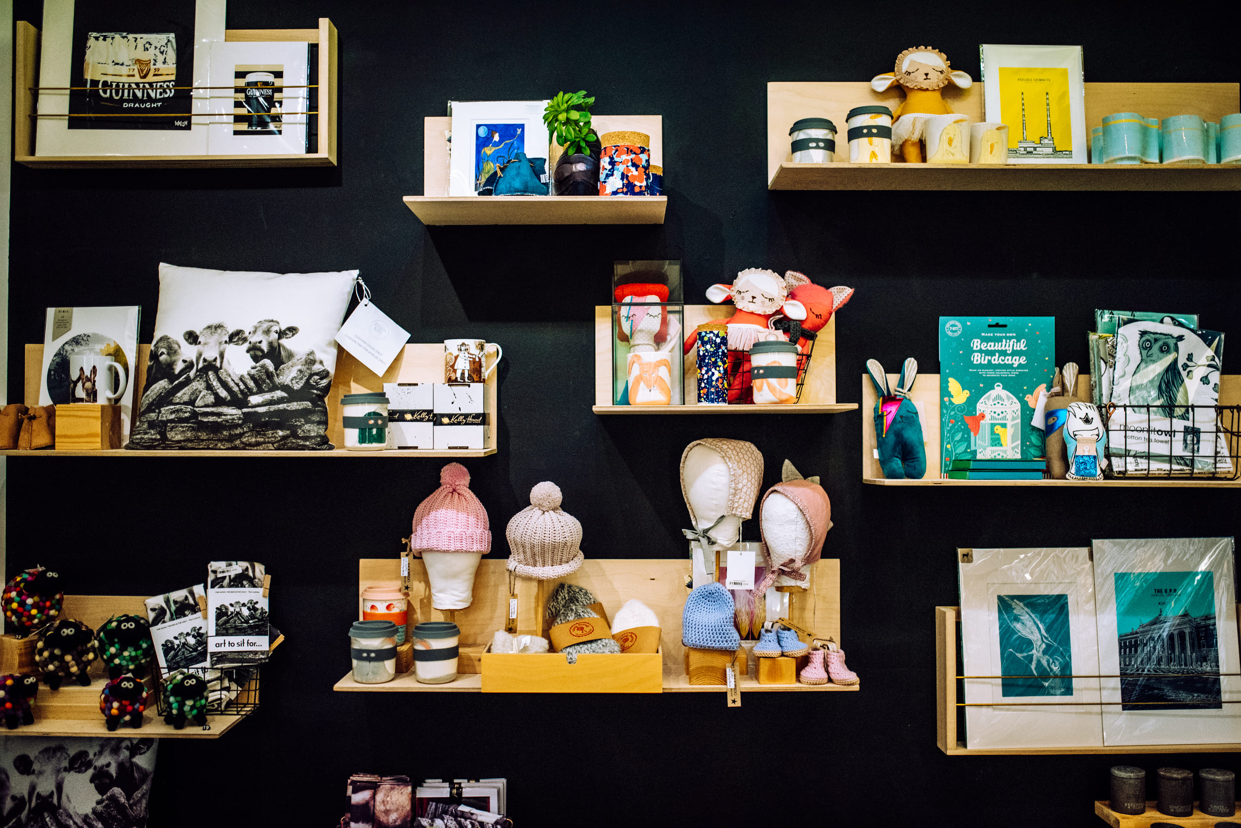 A black wall with wooden shelves. Shelves contain books, knitwear and candles. A variety of objects.